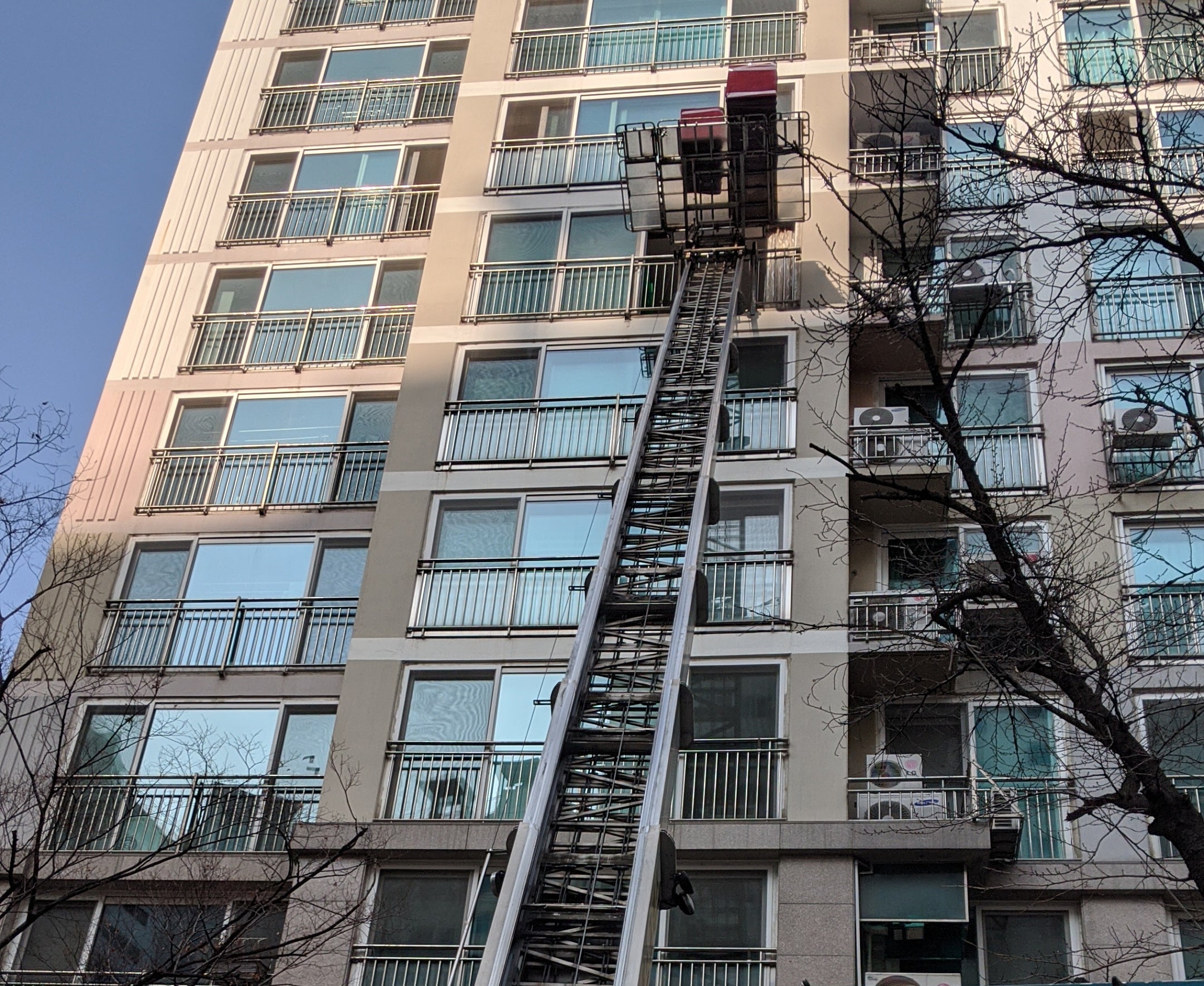 Koreanisches Apartment-Hochhaus von unten fotografiert, an der Fassade ein ausgefahrener Möbellift mit roten Umzugskisten vor einem Balkon