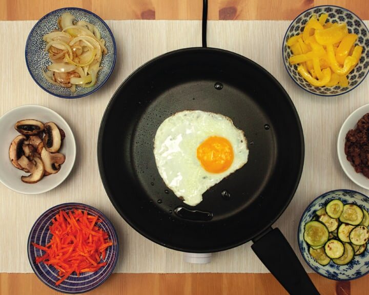 Spiegelei in der Pfanne, ringsum Schälchen mit gebratenem Gemüse und Hackfleisch