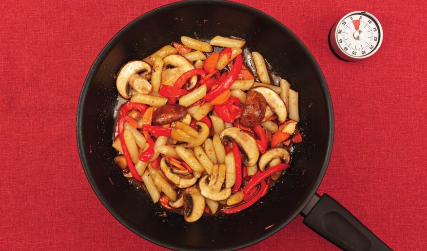 Reiskuchen mit Pilzen und Paprika in einer Pfanne, daneben ein Küchentimer