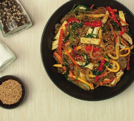 Angerichtetes Japchae mit Sesam, daneben Pfeffermühle und ein Schälchen Sesam