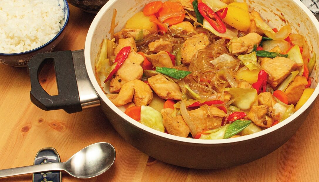 Jjimdak im Topf mit Hähnchen, Glasnudeln, Kartoffeln, Karotten, Weißkohl und roter Chili, daneben eine Schale Reis