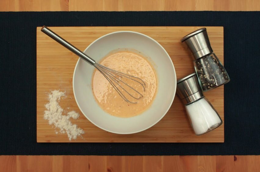 Schüssel mit glattem Teig und Schneebesen, daneben Salz- und Pfeffermühle und etwas Mehl