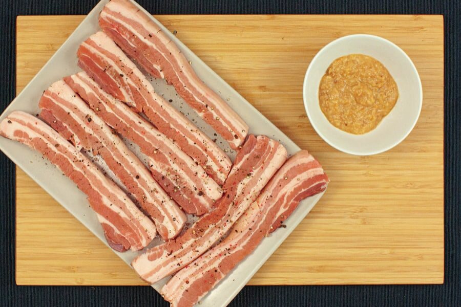 Gepfefferte Schweinebauchstreifen auf einer Platte, daneben ein Schälchen Marinade