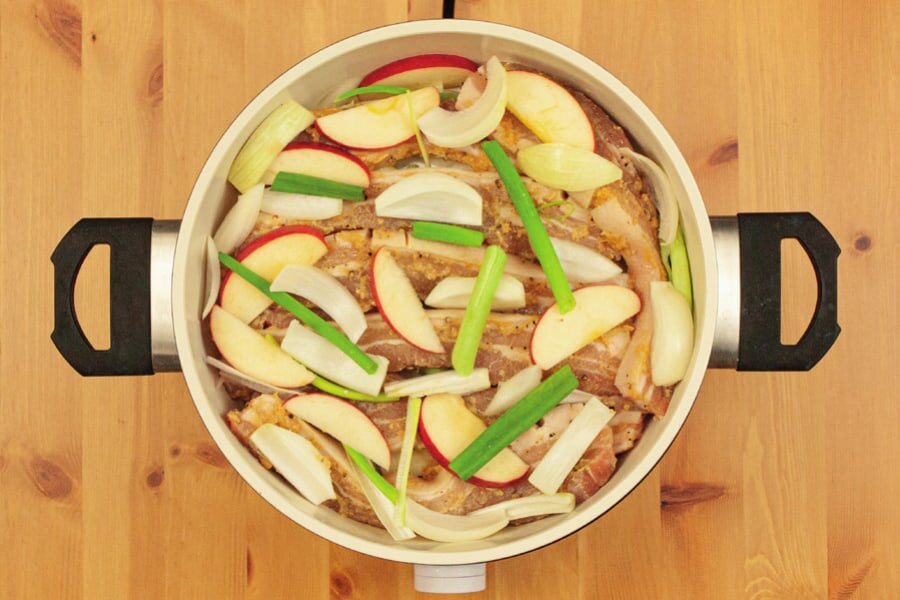 Topf mit Fleisch, bedeckt von Apfel-, Zwiebel- und Frühlingszwiebelstücken