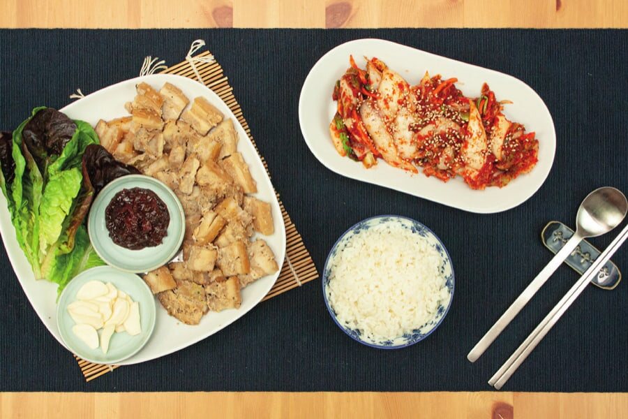 Angerichteter Tisch mit Bossam, Salat, Ssamjang, Knoblauch, Kimchi und Reis