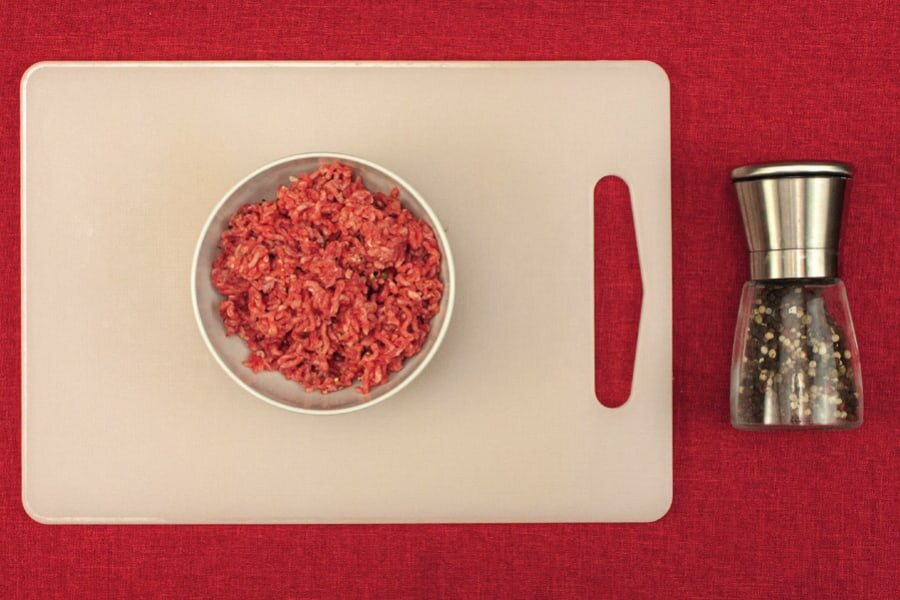 Rinderhackfleisch in einer Schale auf einem Schneidebrett, daneben eine Pfeffermühle