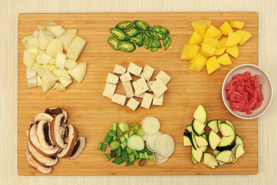 Zwiebel, Chiliringe, Kartoffel- und Tofuwürfel, Pilze, Frühlingszwiebeln und Zucchini auf einem Brett, daneben Rindfleischstreifen