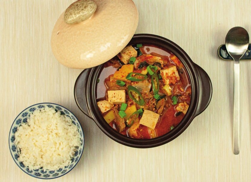 Fertiges Doenjang-Jjigae im Tontopf, daneben Reis und ein Löffel