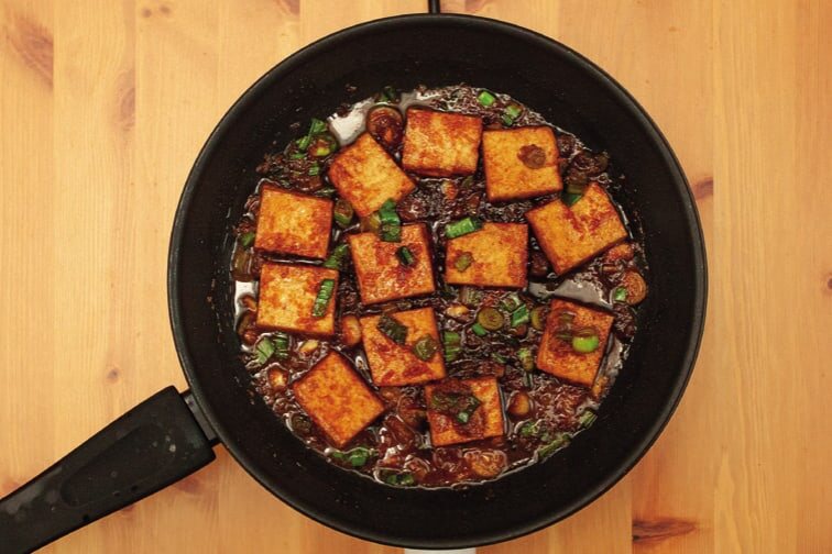 Tofu in eingekochter Soße mit Frühlingszwiebeln in der Pfanne