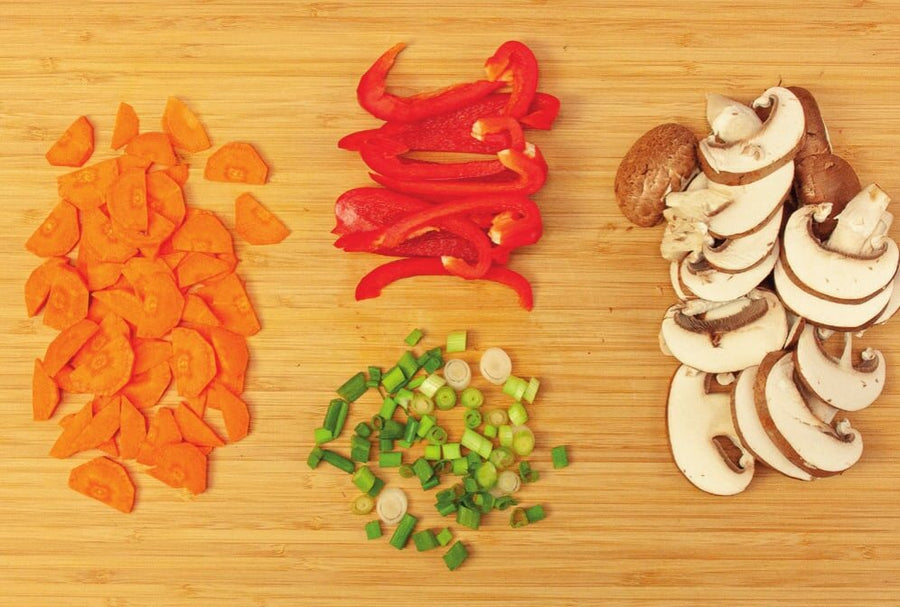 Karottenscheiben, Paprikastreifen, Frühlingszwiebelringe und Champignonscheiben auf einem Holzbrett