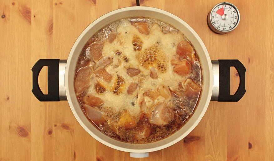 Hähnchenstücke kochen in brauner Soße im Topf, daneben ein Küchentimer
