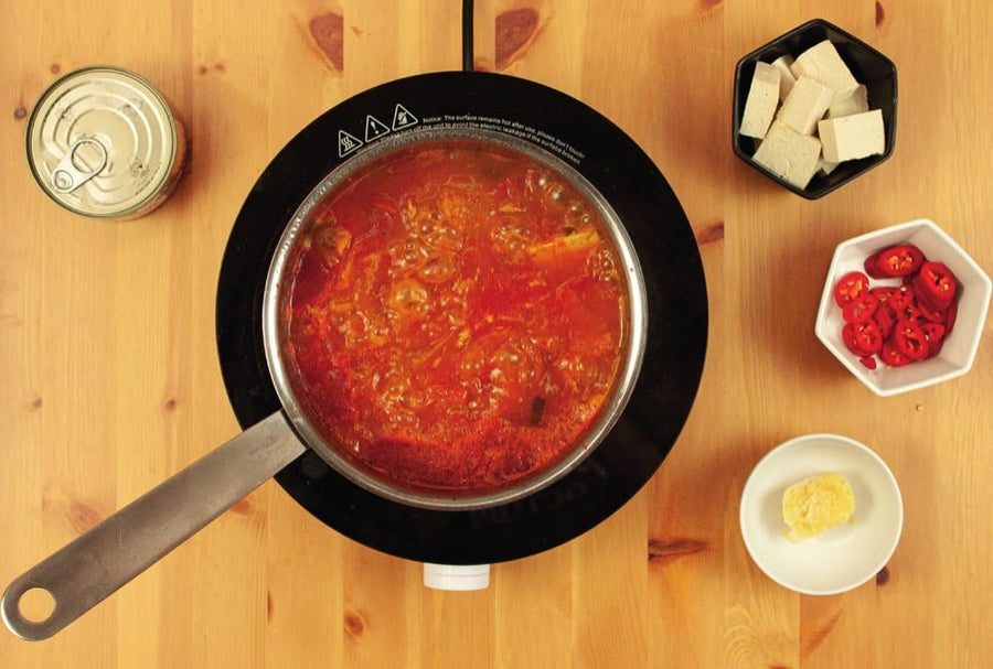 Topf mit Eintopf, daneben Thunfisch, Tofu, Chili und geriebener Knoblauch