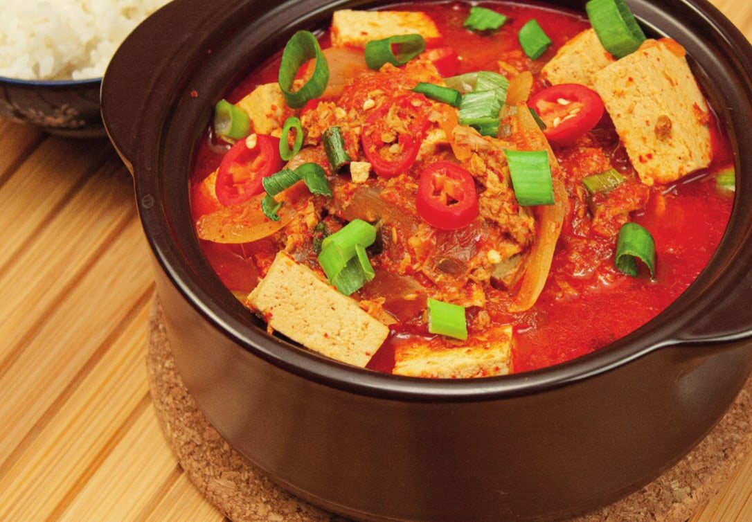 Kimchi-Jjigae im Tontopf mit Tofu, Chili und Frühlingszwiebeln, daneben Reis