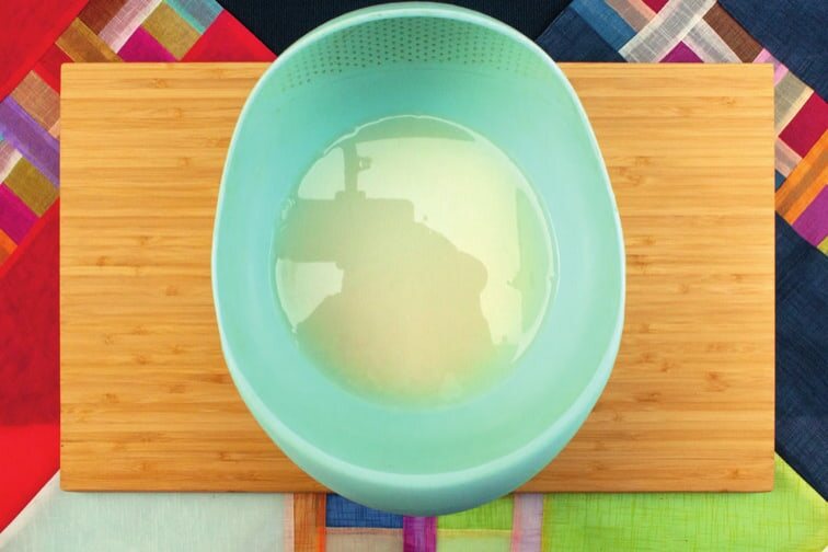 Türkisfarbene Schüssel mit Reis in Wasser auf einem Holzbrett