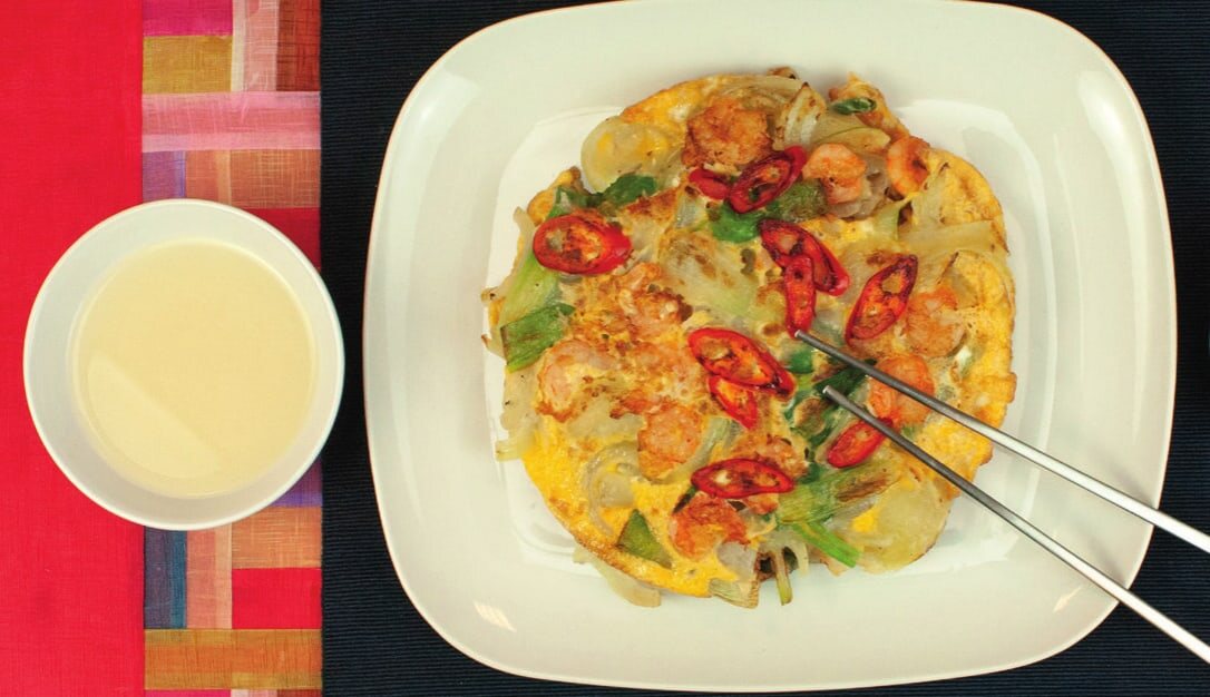 Gebratener Pajeon mit Garnelen und roten Chiliringen, Stäbchen greifen ein Stück