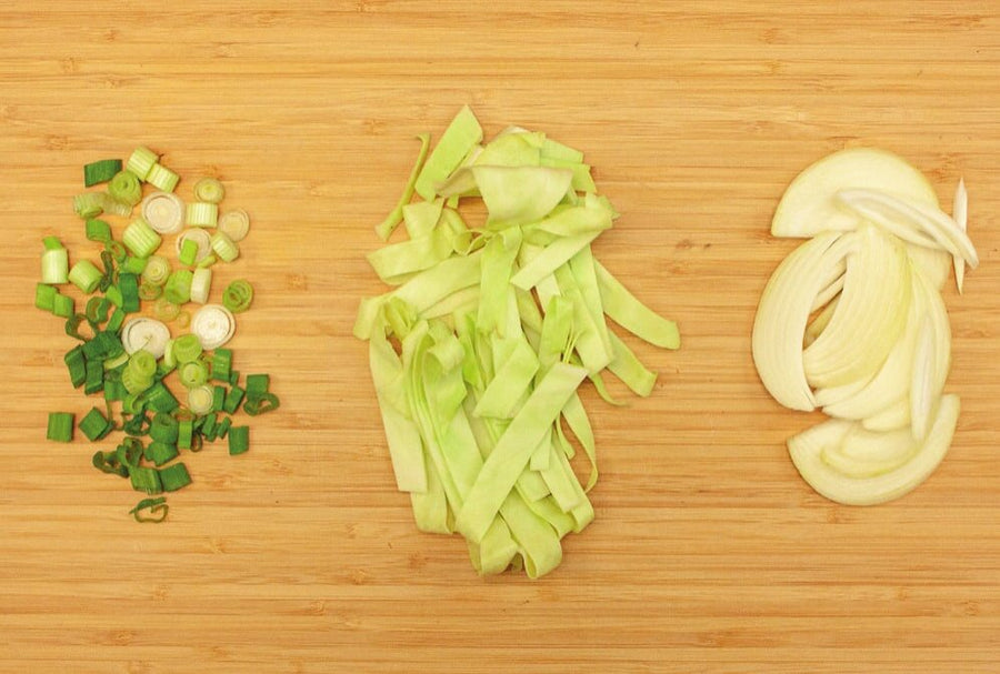 Frühlingszwiebelringe, Weißkohlstreifen und Zwiebelstreifen auf einem Holzbrett